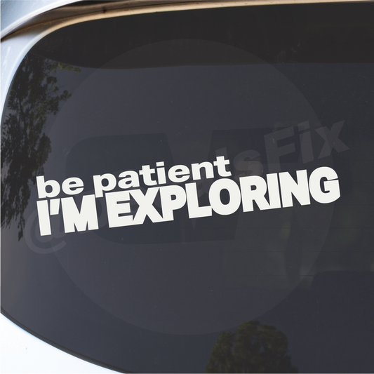 Detail close-up of the Be Patient Im Exploring vinyl decal sticker on a car window, featuring a black and white text design.
