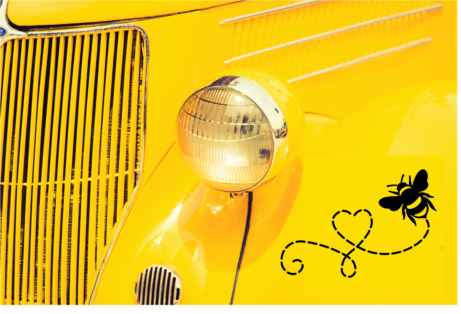Detail view of a yellow vintage car featuring a bee decal on the chrome grille